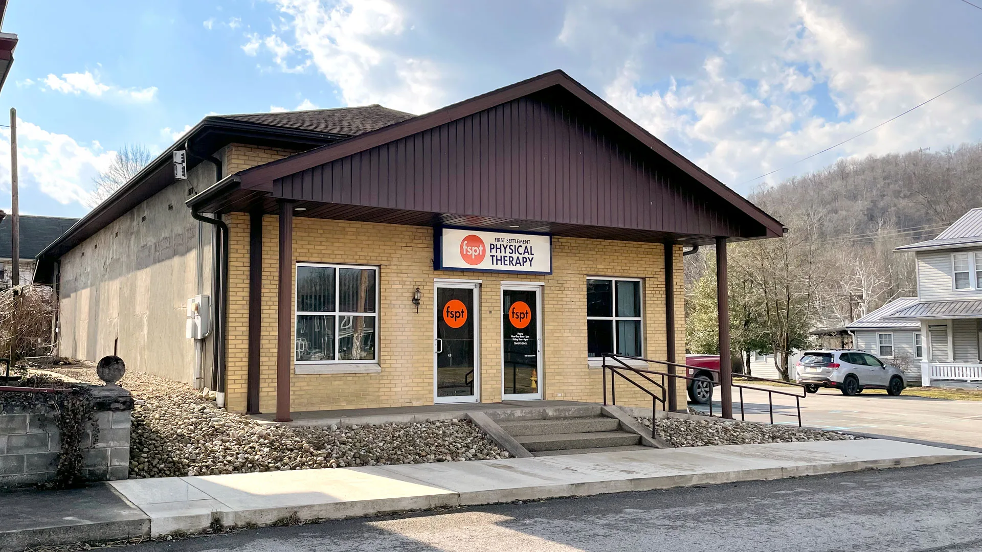 Stone-faced building with a red metal roof and a First Settlement Physical Therapy sign beside the entrance steps