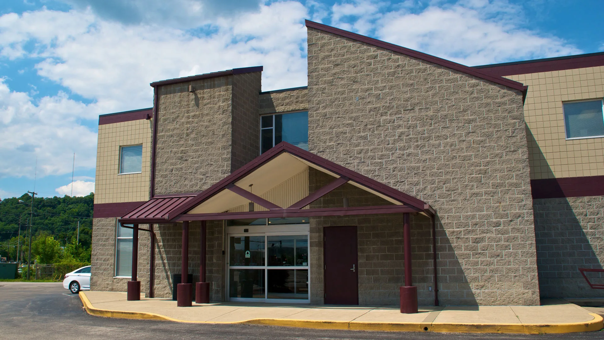 Tan stone building with a red awning entrance and wooded hills rising behind it