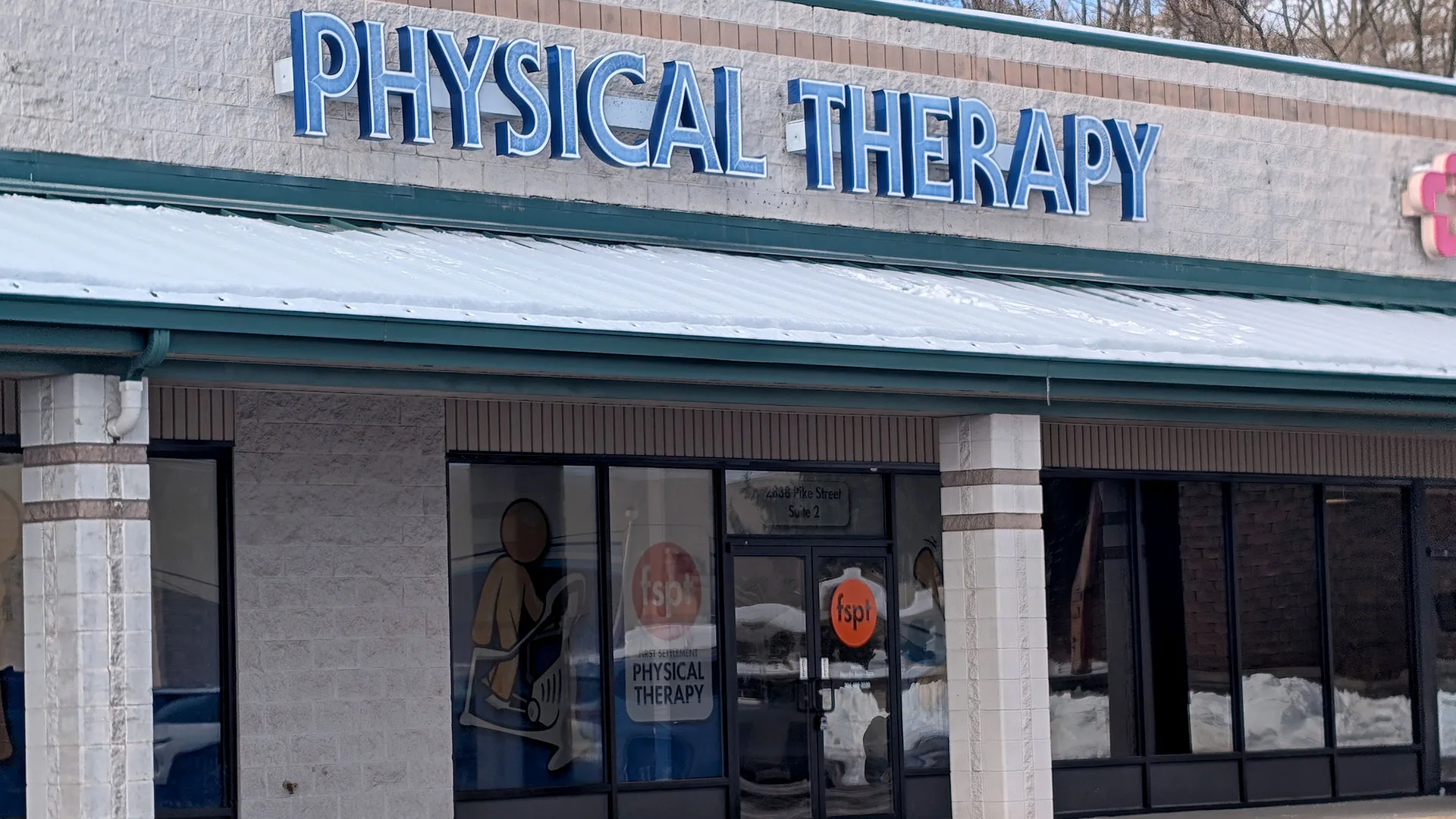 White storefront with large blue PHYSICAL THERAPY lettering above the glass entrance doors
