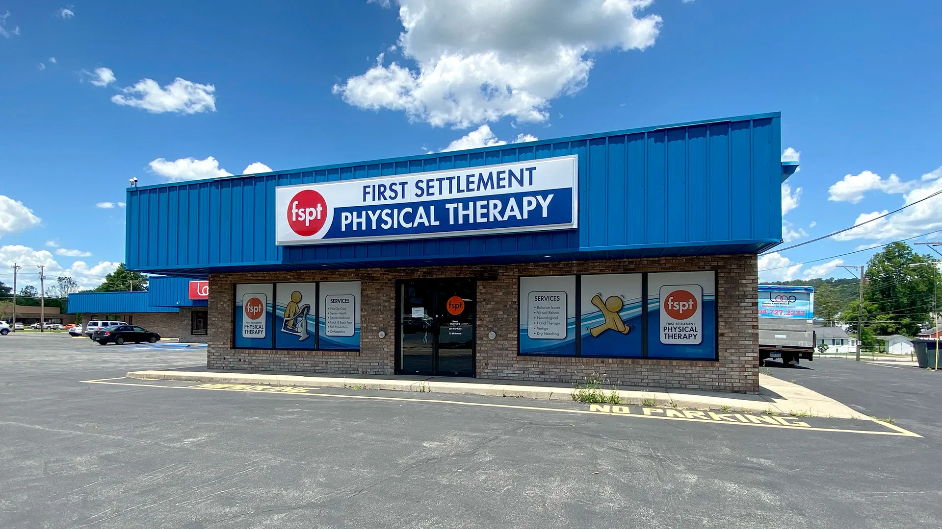 Single-story clinic with a blue roofline sign reading First Settlement Physical Therapy under a clear sky