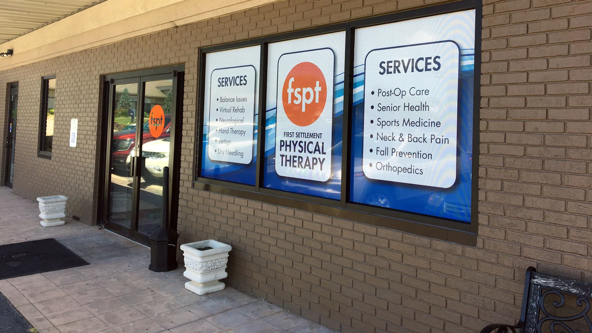 Brick clinic entrance with illuminated window panels listing services including hand care, sports medicine and post-surgical rehabilitation
