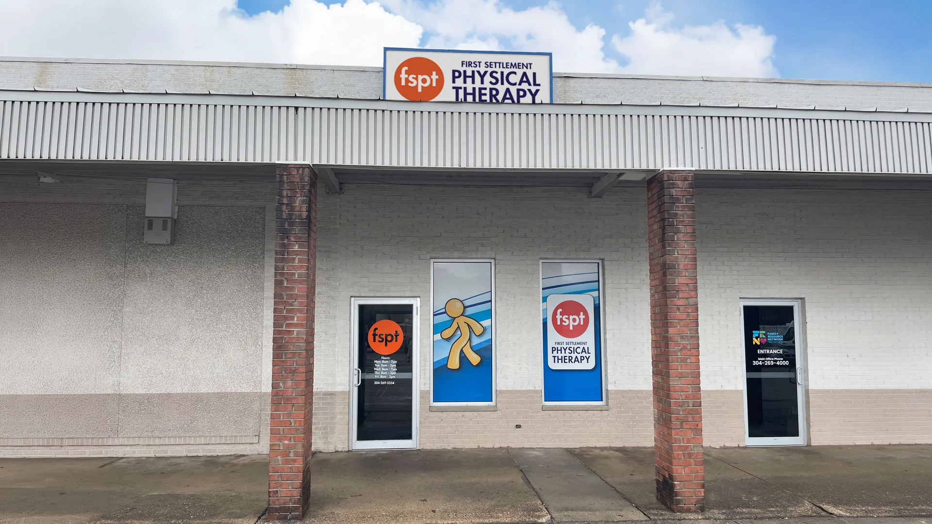 Clinic entrance beneath a covered walkway with brick columns and blue window decals showing the clinic logo
