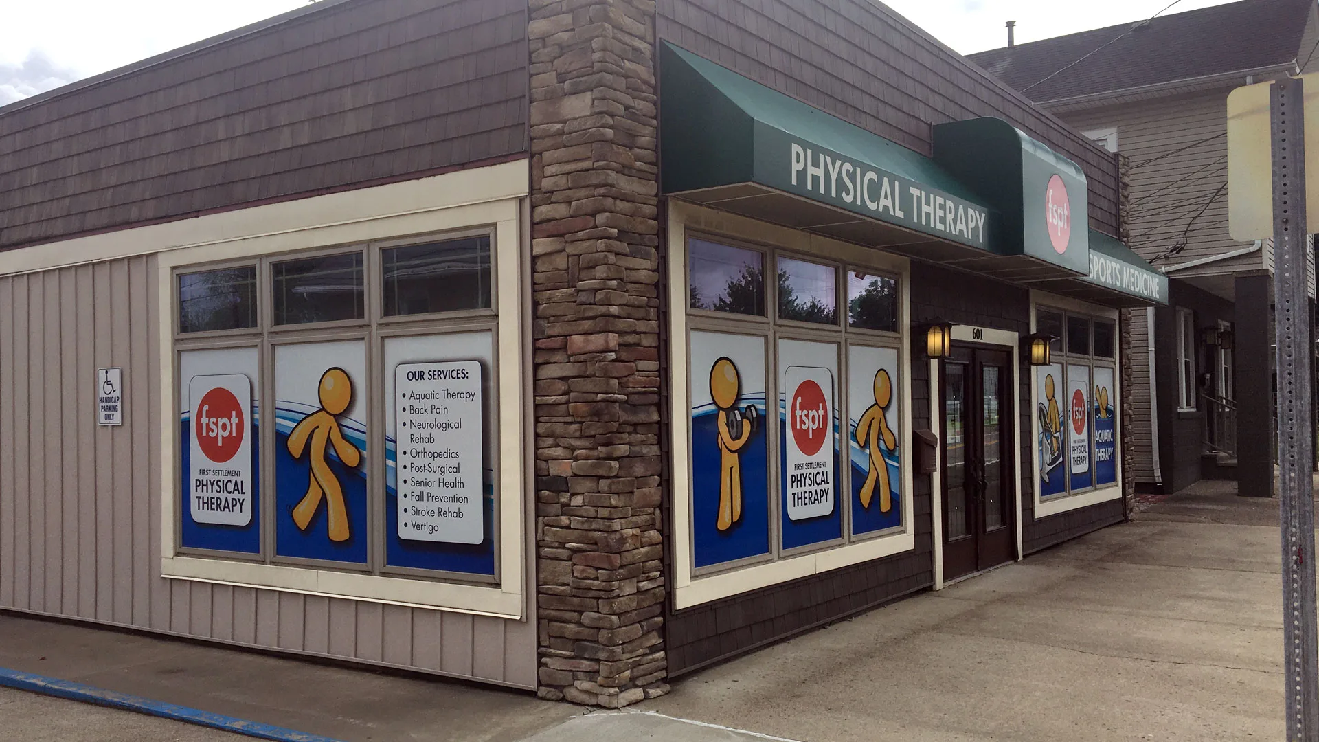 Storefront clinic with a green awning reading Physical Therapy and window panels listing the services offered