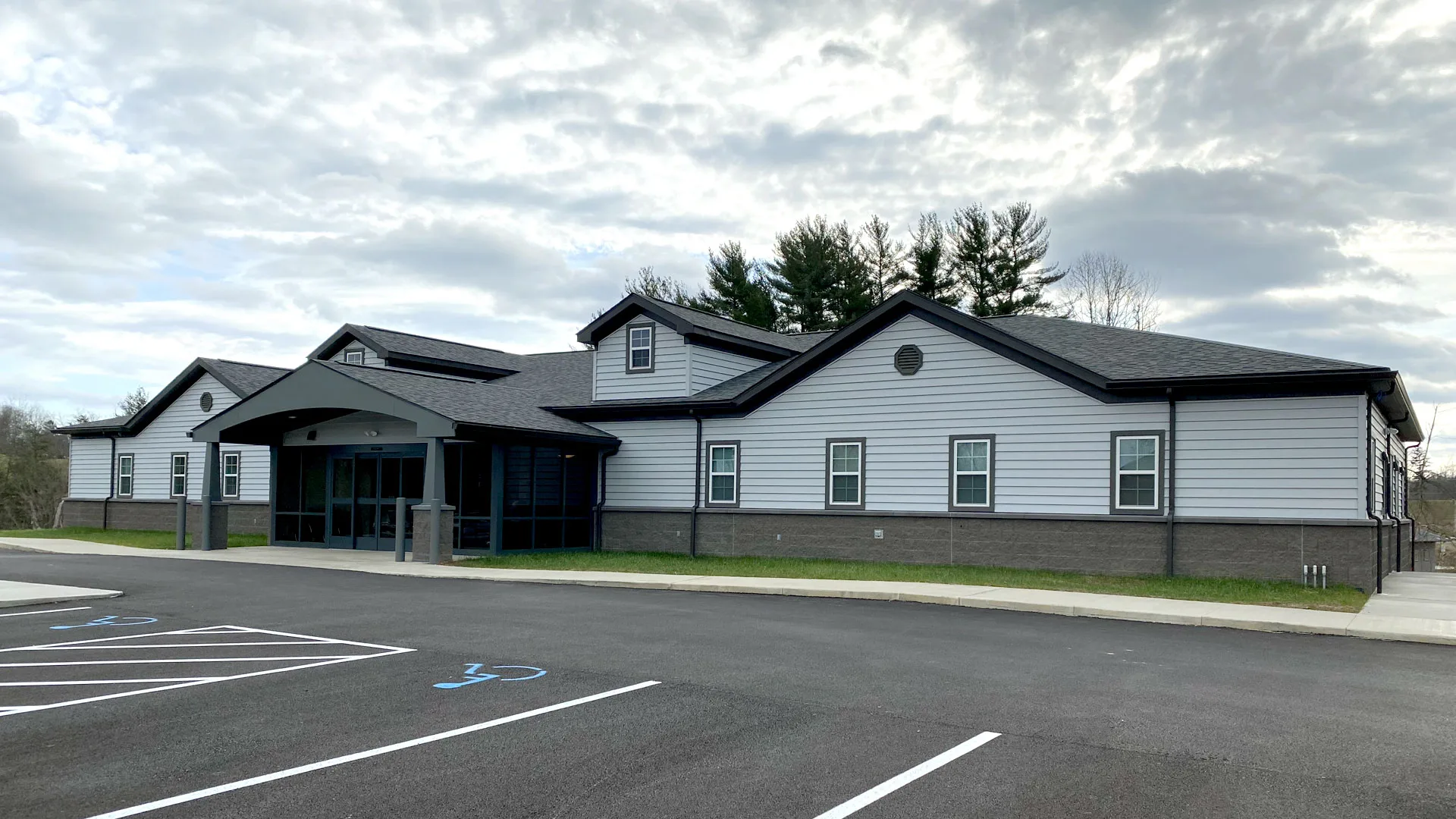 White single-story clinic building with a dark roof and an empty parking lot under a cloudy sky